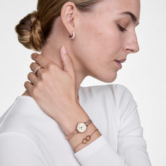 白いトップスを着た女性の手首に、Petite MiniローズゴールドメッシュとElan Unity Braceletを重ね付けしたスタイリングイメージです。小ぶりな文字盤と繊細なチェーンブレスレットが、手元に上品なレイヤードスタイルを演出します。