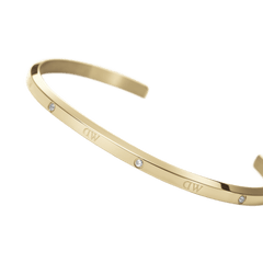Daniel Wellington Classic Lumine Braceletのゴールドカフを近距離で撮影したクローズアップ画像です。滑らかなポリッシュ加工の表面に刻印されたロゴと、ベゼルセッティングで留められたクリスタルの細やかなディテールが際立ちます。