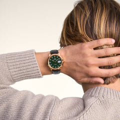 Iconic Sheffield Automatic Rose Goldを着用したスタイリング例。グレーのニットセーターの袖口から覗くエメラルドグリーンの文字盤とブラックレザーストラップが、日常のコーディネートに溶け込んでいます。
