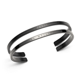 Daniel WellingtonのClassic Bracelet ブラック＆グラファイト2本セット。マットなブラックと明るめのグラファイトのオープンカフを重ね付けしたデザインで、内側にはブランドロゴの刻印が施されたステンレススチール製ブレスレットです。