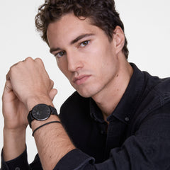 ダークシャツを着た男性がDaniel Wellington Classic Mesh Onyx Blackを着用した様子です。ブラックのメッシュストラップとケースが手首に自然になじみ、落ち着いた装いに調和しています。