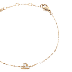 天秤座モデルのCrystal Zodiac Chain Bracelet Goldを斜め上から撮影したクローズアップ画像です。ゴールドの細いチェーンが優美なカーブを描き、中央にはクリスタルであしらわれた天秤座のモチーフが光を反射して繊細に輝いています。右上にはロブスタークラスプ、左上にはブランド刻印プレートとアジャスターリングが確認できます。