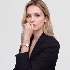ダークジャケットを着た女性が、ツートーンのブレスレットウォッチ、パールスタッドピアス、ゴールドリング、パールチェーンブレスレットを合わせたDaniel Wellingtonのスタイリングイメージです。