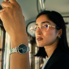 Petite Lumine Bezel 5-Link Arcticを身に着けた女性が、電車のつり革につかまる日常のひとコマ。ブルーのサンレイダイヤルとクリスタルベゼルが自然光に輝き、上品な手元をさりげなく演出します。