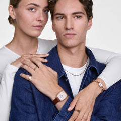 Marlon & Jolie Chain ローズゴールド ペアウォッチセットを着用した男女のスタイリング画像。男性の手首にはブラウンレザーストラップのMarlonが、女性の手首にはローズゴールドチェーンストラップのJolie Chainが映え、デニムと白を基調としたカジュアルなコーディネートに自然に馴染んでいます。