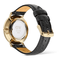 Classic Roman Numerals Date Black Croc Belly Goldを裏蓋側から撮影した画像です。ポリッシュ仕上げのゴールドケース裏蓋にはDaniel Wellingtonのロゴとシリアルナンバーが刻印されており、ブラッククロコベリーレザーストラップの質感やキャメルカラーの裏地、ゴールドのピンバックルが確認できます。