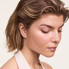ダニエルウェリントンのHoop Earring Rose Goldを着用したモデルの横顔。ローズゴールドのフープピアスが耳たぶに自然になじみ、上部にはクリスタルスタッドピアスを重ね付けしたスタイリング例です。
