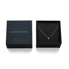 Daniel Wellingtonのロゴ入りネイビーギフトボックスに収められたMirelle Solitaire Necklace Silver。黒いクッショニングの上に、繊細なシルバーチェーンと一粒のジルコニアペンダントが美しく配置されています。贈り物にぴったりの上品なパッケージです。
