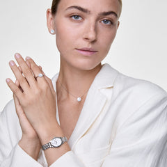 Audrey Earrings Mother of Pearl Silverを着用したスタイリングイメージです。同コレクションのネックレスやリング、シルバーの腕時計と合わせ、マザーオブパールのトーンで統一感のあるコーディネートに仕上げています。