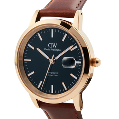 Iconic St Mawes Automatic Rose Goldを斜めから捉えたクローズアップ画像です。ブラックダイヤルにローズゴールドの夜光インデックスと針が映え、3時位置の日付拡大窓の細部まで確認できます。ブラウンレザーストラップとの調和も美しく際立っています。