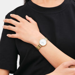Petite Roman Numerals 5-Link Goldを身に着けた女性の手元です。ブラックのトップスに映えるゴールドの5連ブレスレットと、ローマ数字インデックスのホワイトダイヤルが、手首に上品なアクセントを添えています。