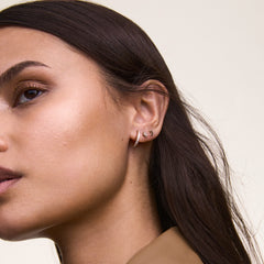 クリスタルが輝くゴールドフープピアス「Crystal Hoop Earring Gold」を着用した耳元のアップです。ムーンスタッドやスターモチーフのピアスと重ねづけし、華やかな印象に仕上げたスタイリング例をご紹介します。