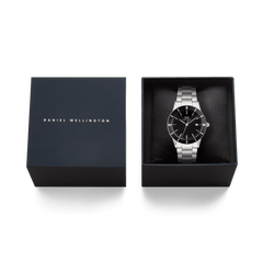 Daniel Wellingtonのネイビーのブランドロゴ入りギフトボックスに、クッションで包まれたIconic Paradigma Link Black Enamelを収めた様子を上から撮影した画像です。贈り物にぴったりの上品なパッケージングがご覧いただけます。
