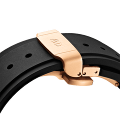 Switch Rose Goldのローズゴールド製デプロイメントバックル部分を拡大した画像です。バックル表面にはDaniel Wellingtonのロゴが刻印されており、半開きの状態でヒンジや固定ピンの精密な構造が確認できます。ブラックFKMラバーストラップのしなやかな質感との組み合わせも印象的です。
