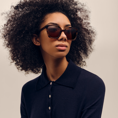 Daniel WellingtonのGrande Bio-Acetate Brown Demiを着用した女性のスタイリングイメージです。ネイビーのニットポロシャツにべっ甲柄のオーバーサイズスクエアフレームが映え、落ち着いた大人の雰囲気を演出しています。