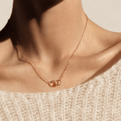 ダニエルウェリントン Elan Unity ネックレスを着用した女性の胸元。ローズゴールドのケーブルチェーンが鎖骨に沿って優雅に輝き、2つのインターロッキングリングがクリーム色のニットの上で上品に映えます。