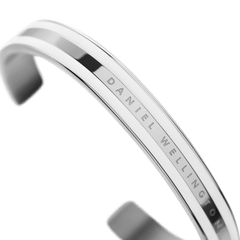 Emalie Braceletシルバーを斜め上から捉えた画像です。ホワイトエナメルを挟んだポリッシュシルバーの3本ライン構造と、中央のバンドに刻まれたDaniel Wellingtonのロゴが確認できます。カフ型の開口部も見えます。