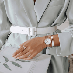 ライトグレーのジャケットを着た女性の手元に、Daniel WellingtonのIconic Link Rose Goldを合わせたスタイリングです。ローズゴールドのブレスレットやリングと重ね付けし、統一感のあるコーディネートに仕上げています。