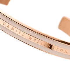 Emalie Bracelet Desert Sand Rose Goldのロゴ部分をマクロ撮影した画像です。ローズゴールドのポリッシュ仕上げフレームに刻まれたDaniel Wellingtonの文字と、隣接するデザートサンドカラーのエナメル面の滑らかな質感が鮮明に捉えられています。