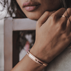 エミリー ブレスレット Dusty Rose Rose Goldを手首に着けたモデルのクローズアップです。ダスティローズのエナメルとローズゴールドの3本ラインが肌になじみ、同系色のリングとも自然に調和しています。