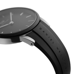 Iconic Motion Silverのケースとストラップの接続部分を横から捉えたクローズアップ画像です。ブラックのベゼルからシルバーのケースサイドへの切り替えが際立ち、FKMラバーストラップにはDaniel Wellingtonのブランド名が型押しされています。