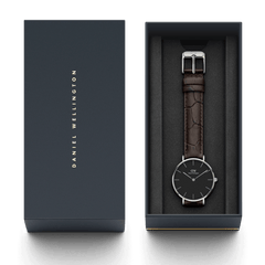 Petite York Black Silverがダークネイビーのブランドギフトボックスに収められています。ブラックの文字盤とダークブラウンのクロコダイルエンボスレザーストラップが、クッション素材に包まれて美しく映え、贈り物にふさわしい上品な仕上がりです。