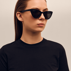 ブラックのトップスにDaniel WellingtonのLynx Bio-Acetate Blackを合わせた女性モデル。キャットアイシルエットが顔立ちに凛とした印象を添え、テンプル部分にはゴールドのブランドロゴがあしらわれています。