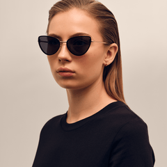 Daniel Wellington Lynx Steel Blackを着用した女性モデルの斜めアングル写真です。ブラックのクルーネックトップスにキャットアイシルエットのサングラスを合わせ、ローズゴールドの細身テンプルが横顔に沿うスタイリングが特徴です。