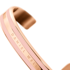 エミリー ブレスレット Dusty Rose Rose Goldを斜めから捉えた画像です。カフの優美な曲線とダスティローズのエナメル、そしてローズゴールドのポリッシュ仕上げが生み出す光沢のコントラストが際立ちます。中央のバンド部分にはDaniel Wellingtonの刻印が施されています。