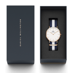 Classic Glasgow Rose Goldが、ダークネイビーの専用ギフトボックスに収められています。箱の蓋にはゴールドのDaniel Wellingtonロゴが縦に刻印され、内側にはネイビーとホワイトのNATOストラップを装着した腕時計が丁寧にセットされており、贈り物にぴったりの上品なパッケージです。