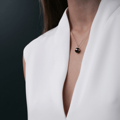 白いVネックブラウスの胸元に、Aspiration Necklace Rose Gold Blackを合わせたスタイリングイメージです。ブラックセラミックの球体ペンダントが鎖骨のやや下に自然になじみ、白い生地とのコントラストが美しく引き立ちます。