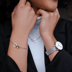 Elan Unity Braceletのシルバーを着用したスタイリング例です。右手首にはブレスレットを、左手首にはシルバーメッシュストラップの腕時計を合わせ、首元にはElan Unity Necklaceを重ねています。シルバートーンで統一した上品なコーディネートです。