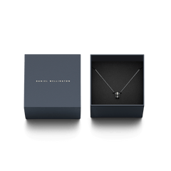 Emalie Necklace Silver Blackが、ダークネイビーのDaniel Wellingtonブランドボックスに収められたギフトパッケージです。箱の蓋にはブランドロゴが箔押しされ、ブラックエナメルのリングペンダントとシルバーチェーンが黒いクッションカバーの上に丁寧にセットされています。