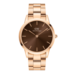Daniel Wellington Iconic Link Amberを正面から捉えた商品画像です。アンバーカラーのサンレイ文字盤は中心から深いブラウンへと広がり、ローズゴールドの細身の針とバーインデックスが落ち着いた色調の中で控えめながら存在感を放っています。ケース右側にはローズゴールドのリューズが配置され、ポリッシュとサテン仕上げを組み合わせたリンクブレスレットが上下に伸びる構図となっています。