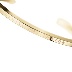 Classic Bracelet Goldのロゴ刻印部分をクローズアップした画像です。ポリッシュ仕上げのゴールドカフ表面に、Daniel Wellingtonの文字が繊細に刻印されているディテールがご覧いただけます。