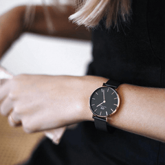ブラックのトップスを着た女性がPetite Ashfield Rose Goldを手首に着用したスタイリング写真です。ブラックの文字盤とローズゴールドのケースのコントラストが、マットブラックのメッシュストラップと調和し、シックな装いに自然になじんでいます。