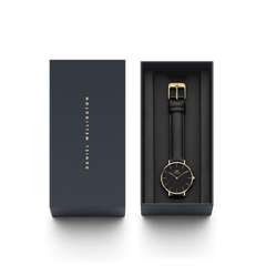 Petite Sheffield Black Goldが、ダークネイビーの専用ギフトボックスに収められた様子です。ブラックレザーストラップとゴールドケースの腕時計が、黒いクッションの上に丁寧にセットされており、贈り物にぴったりの上品なパッケージとなっています。