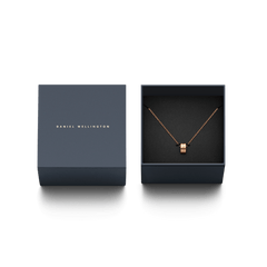 Elan Necklace ローズゴールドが、Daniel Wellingtonのネイビーのギフトボックスに収められています。箱の蓋にはゴールドのブランドロゴが箔押しされ、黒いクッションケースの上にリングモチーフのペンダントとケーブルチェーンが丁寧にセットされています。