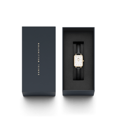 Daniel Wellingtonのブランドロゴが箔押しされたネイビーカラーのギフトボックスに収められたQuadro Pressed Sheffield Gold。ブラックのクッショントレイに、ゴールドケースとブラックレザーストラップの腕時計が美しく配置されており、贈り物にぴったりの上品なパッケージです。