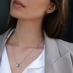 エラン ネックレス シルバーを着用した女性のクローズアップです。白いシャツとベージュのジャケットの胸元に、小ぶりなリングペンダントが自然になじんでいます。同シリーズのシルバーピアスと合わせたコーディネートもご覧いただけます。