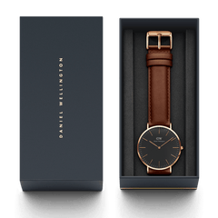 クラシック St Mawes Black Rose Goldが、ダークネイビーの専用ギフトボックスに収められた状態です。ブラックの文字盤とダークブラウンのレザーストラップをあしらった腕時計は、起毛素材のインナーに丁寧にセットされ、贈り物にぴったりの上品なパッケージングとなっています。