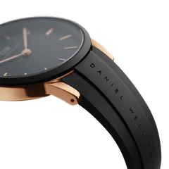 Iconic Motion Rose Goldを横から捉えたクローズアップ画像です。マットブラックのベゼルとローズゴールドケースのコントラストが、薄型プロファイルをより際立たせています。FKMラバーストラップの表面には、Daniel Wellingtonの刻印が縦に入っています。