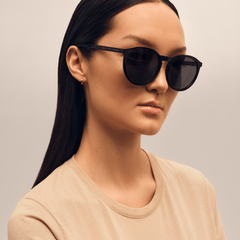 Daniel WellingtonのArch Bio-Acetate Blackを着用した女性モデル。ラウンド型のブラックフレームが顔になじみ、テンプル部分にはゴールドのブランドロゴが控えめにあしらわれています。