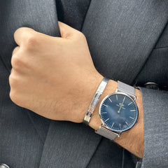 グレーのスーツを着た男性の手首に、Elan Braceletシルバーとメッシュストラップの腕時計を重ね付けしたスタイリング。ビジネスシーンにも違和感なく馴染む着用イメージです。