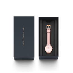 Daniel WellingtonのPetite Cherry Blossomが、ネイビーのギフトボックスに収められています。箔押しのブランドロゴが施された蓋と、黒いクッションの上にピンクのレザーストラップとローズゴールドケースの本体が並び、贈り物にぴったりの上品なパッケージです。